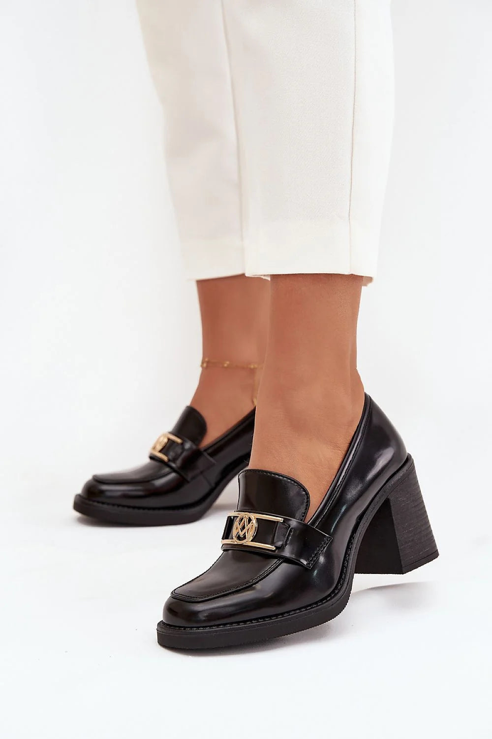 Black patent leather loafers with block heel and gold buckle detail on model.