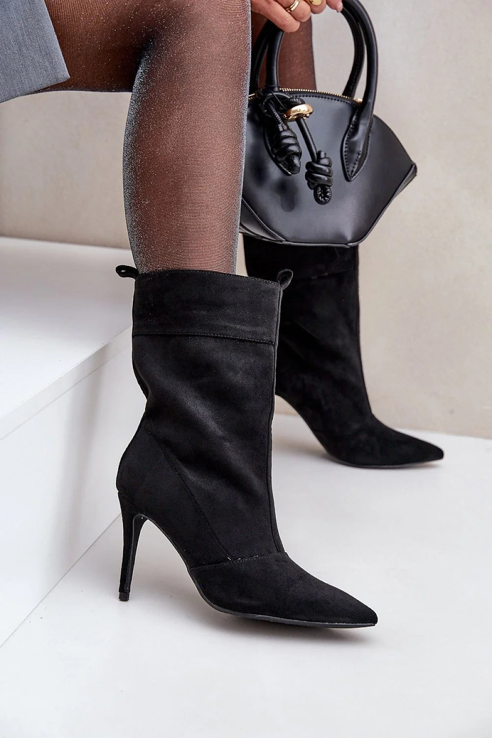 Black suede pointed-toe heeled boots with a structured black handbag.