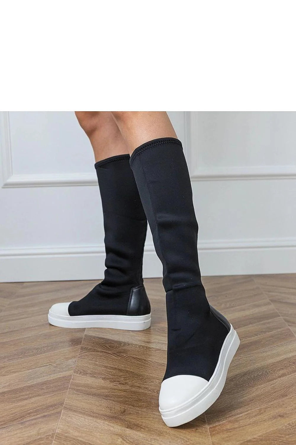 Black knee-high boots with white cap toes and platform soles, on a wooden floor.