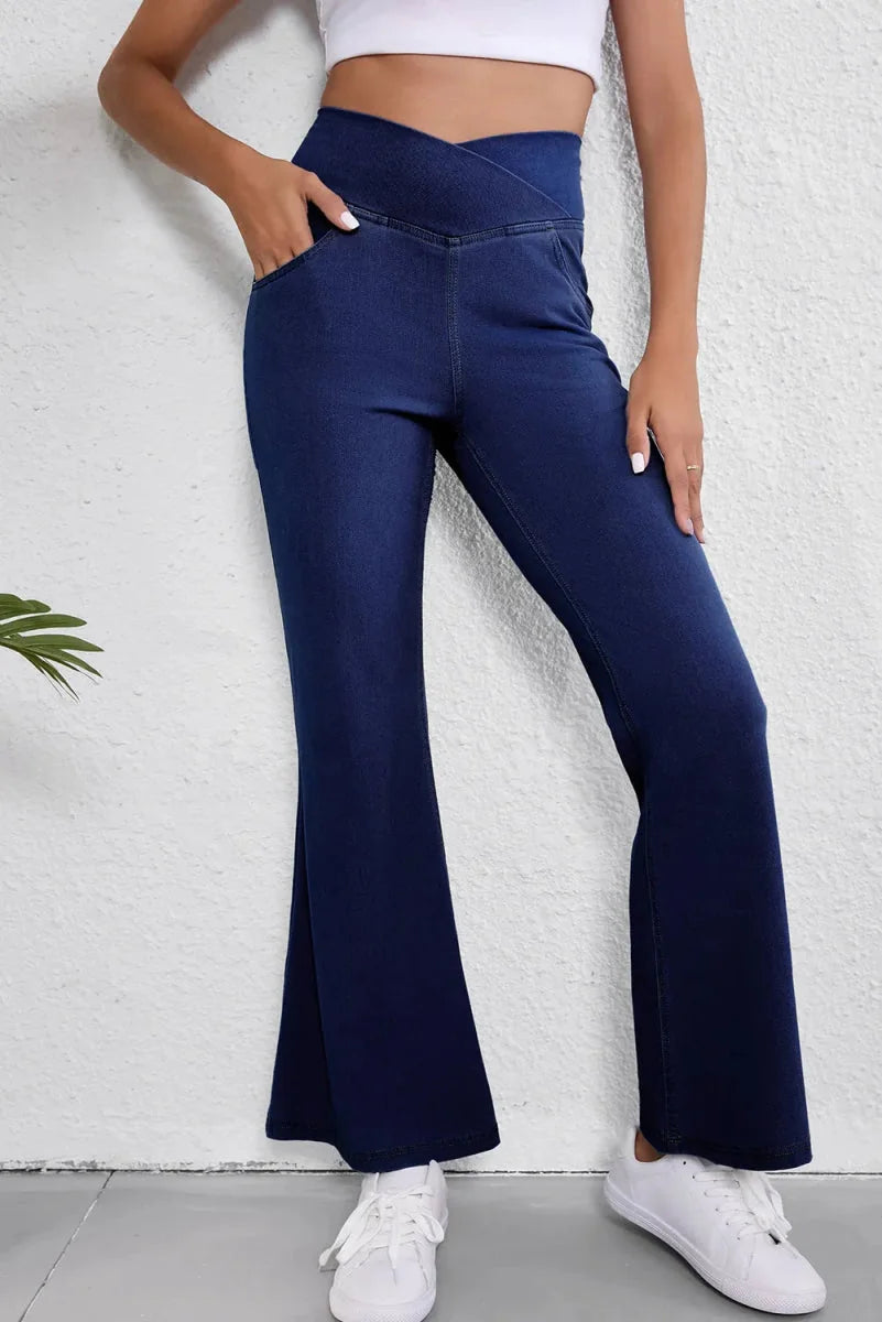 Navy blue denim flare pants with a crossover waistband and moderate stretch, worn by a model.