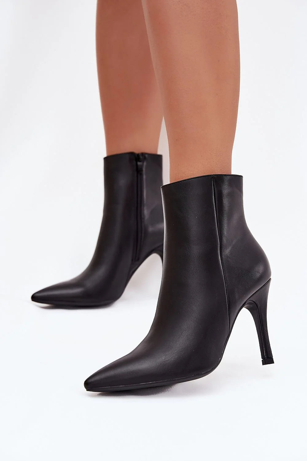 Black leather pointed-toe stiletto ankle boots with side zippers on model.