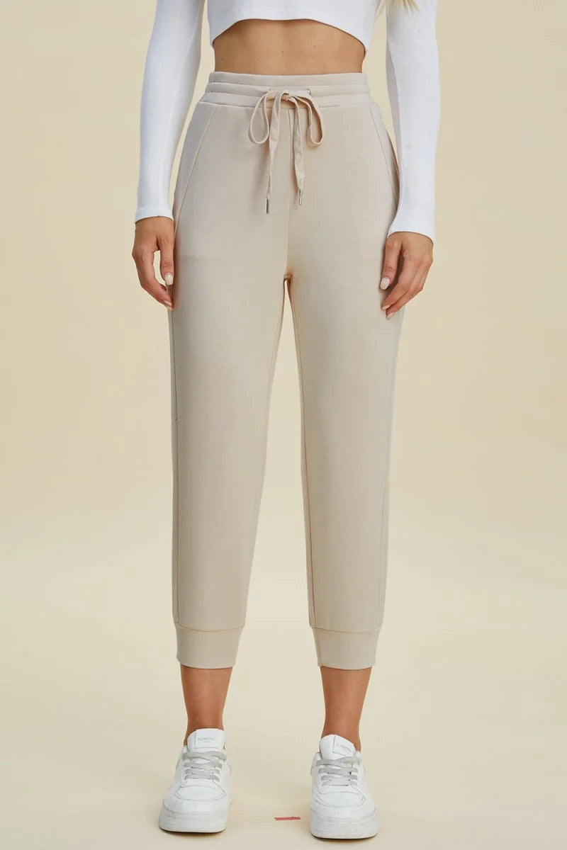 Beige cropped joggers with drawstring waist and cuffed ankles, on model.