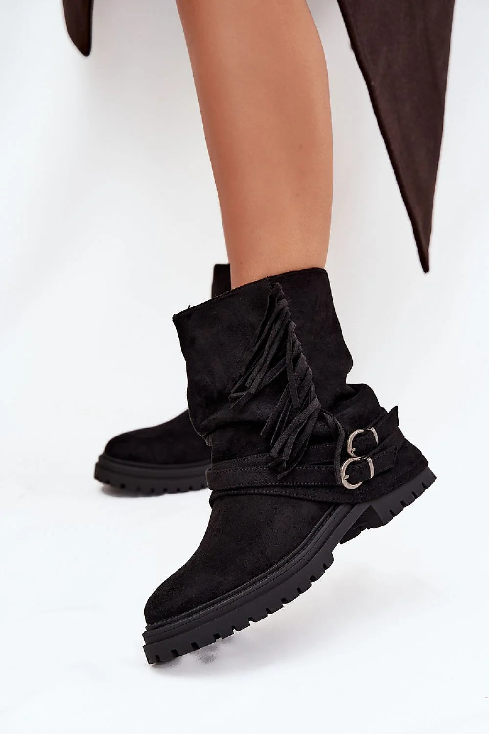 Black suede slouchy ankle boots with fringe and buckle straps on model.