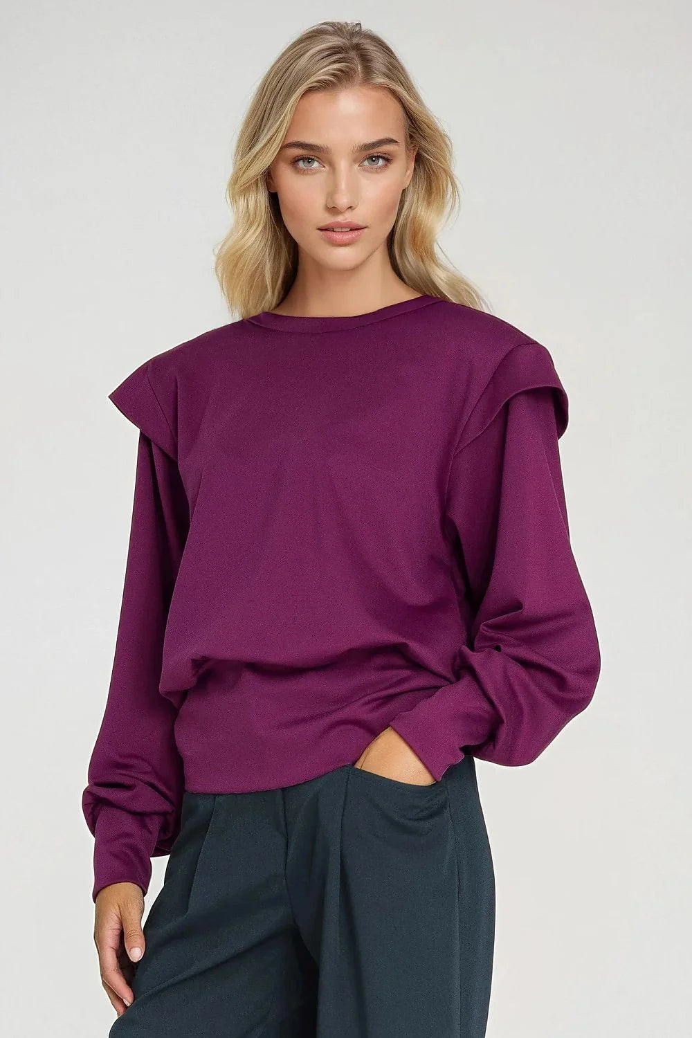 Woman in a deep purple long-sleeved top with layered shoulders, paired with dark gray wide-leg pants.