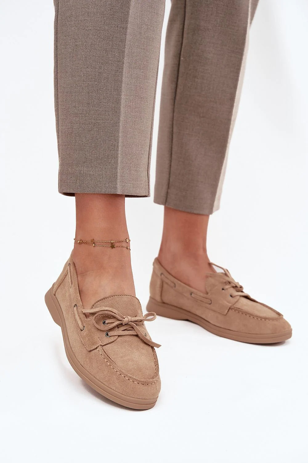 Close-up of tan suede slip-on loafers with a bow detail and an anklet.