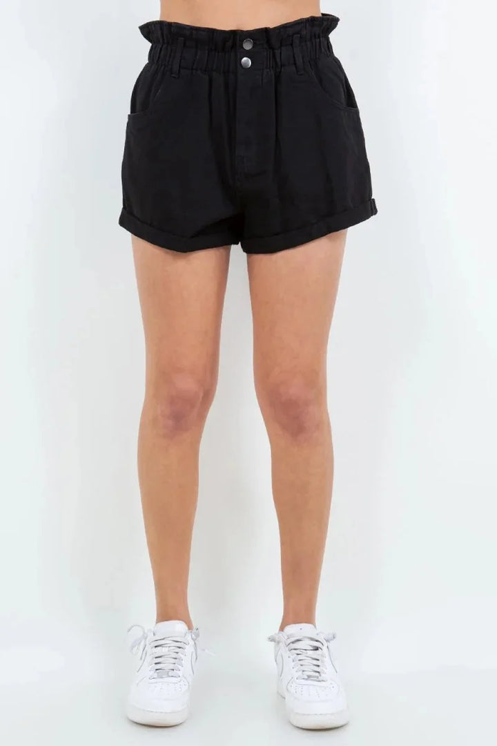 Black denim shorts with a ruffled high waist, two front buttons, and cuffed hems, shown on a model.