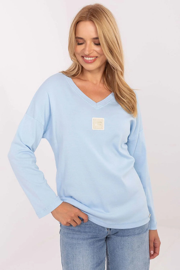 Light blue long-sleeve v-neck top with a relaxed fit and square logo patch on the chest.