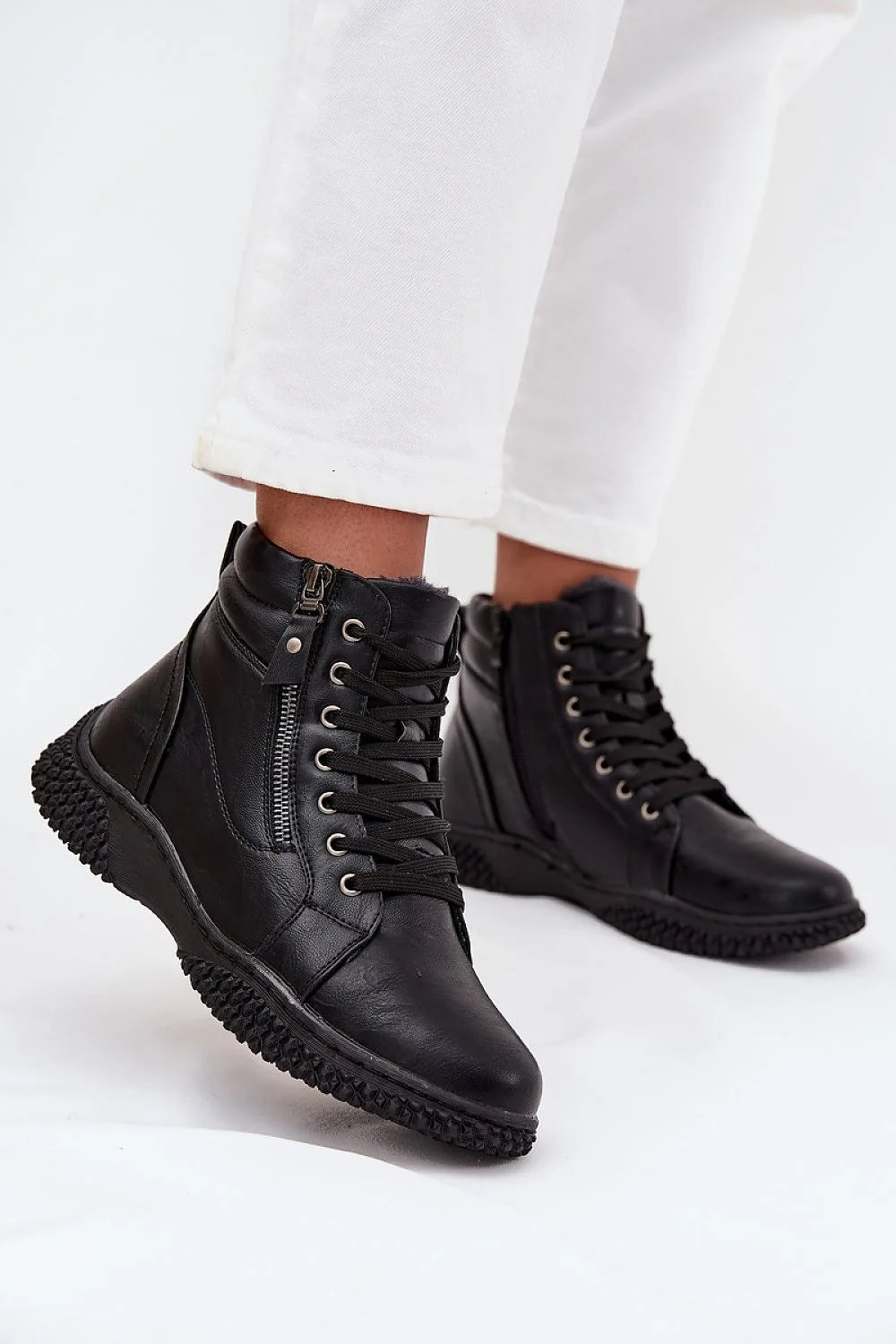 Black leather lace-up boots with side zipper detail and shearling trim on model wearing white pants.