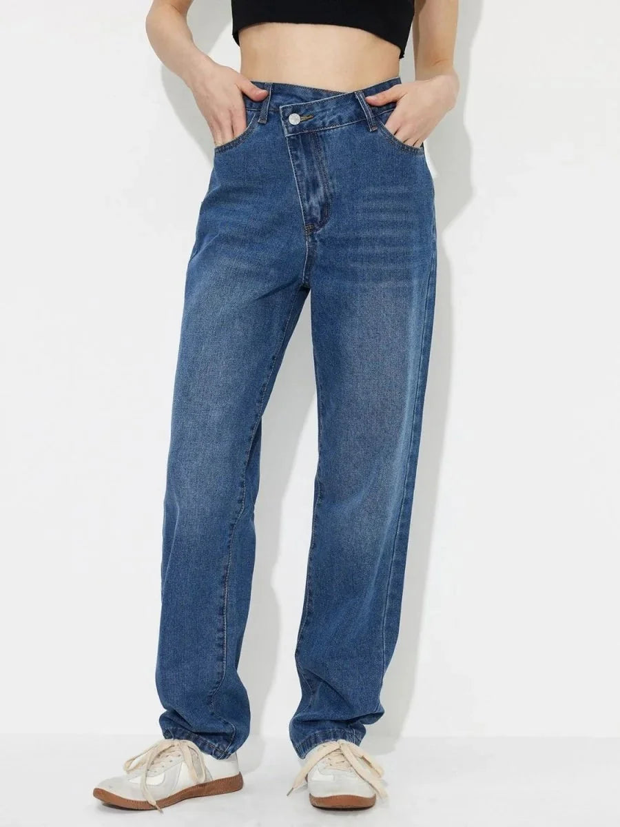 Medium wash denim jeans with a unique crossover waistband and a relaxed fit.
