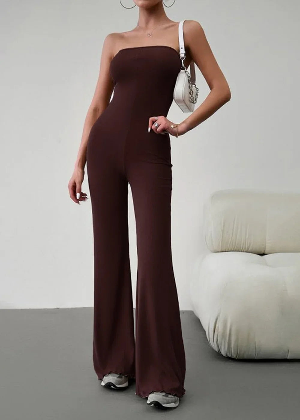Brown strapless wide-leg jumpsuit with a ruched hem, worn by a model with a white purse.