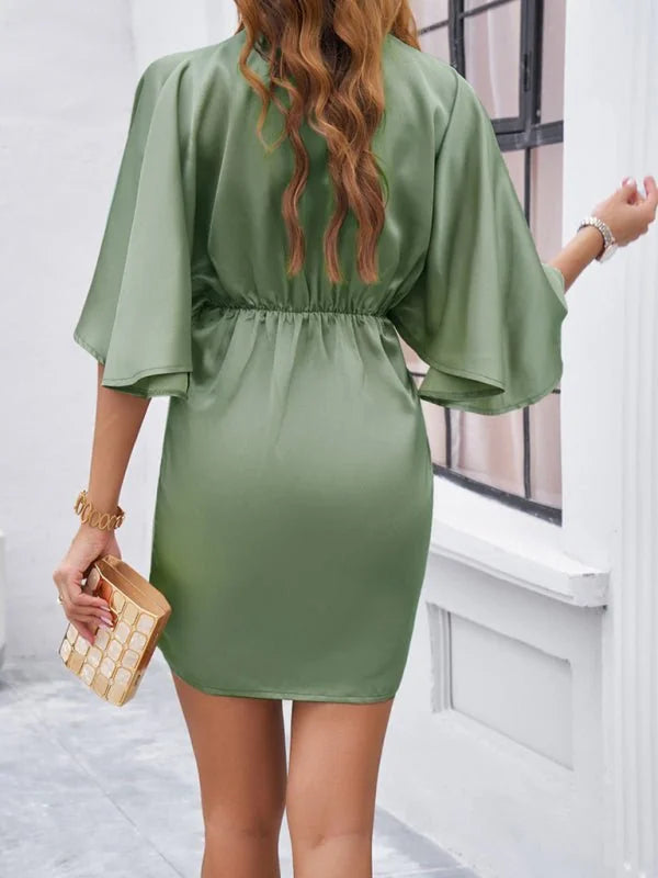 Satin olive green mini dress with wide sleeves, cinched waist, and a gold clutch.