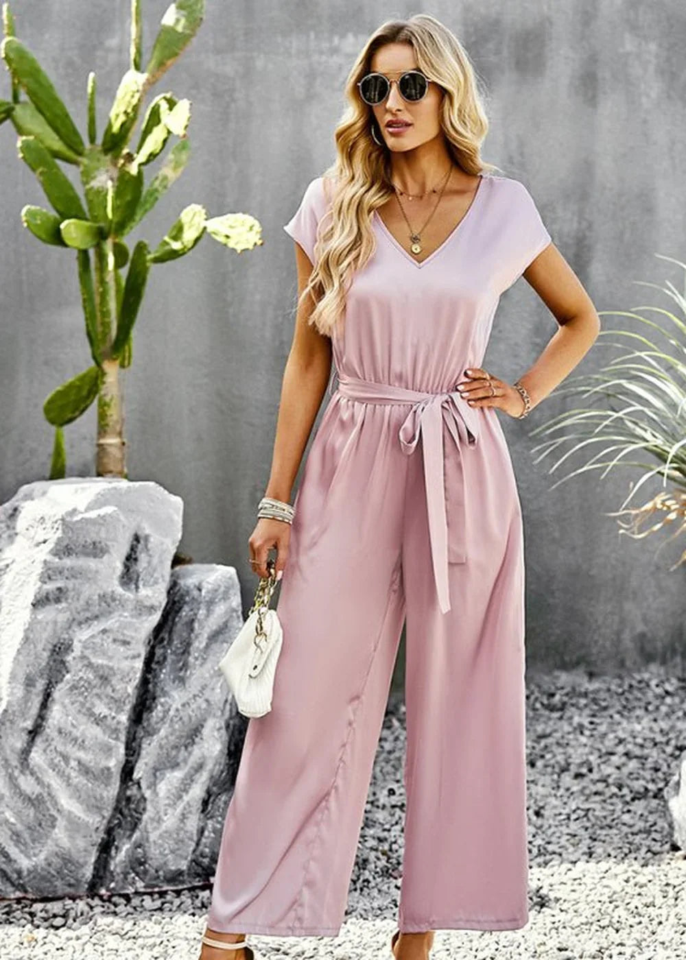 Satin mauve jumpsuit with V-neck, tie waist, and wide legs, held by a model.