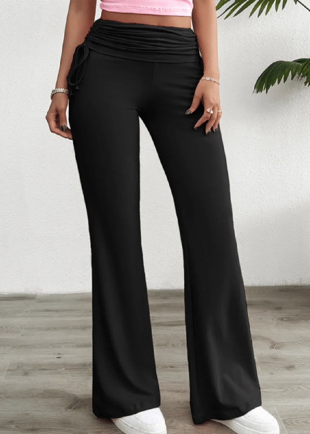 Black wide-leg pants with ruched drawstring waist and flared leg opening, worn with white sneakers.
