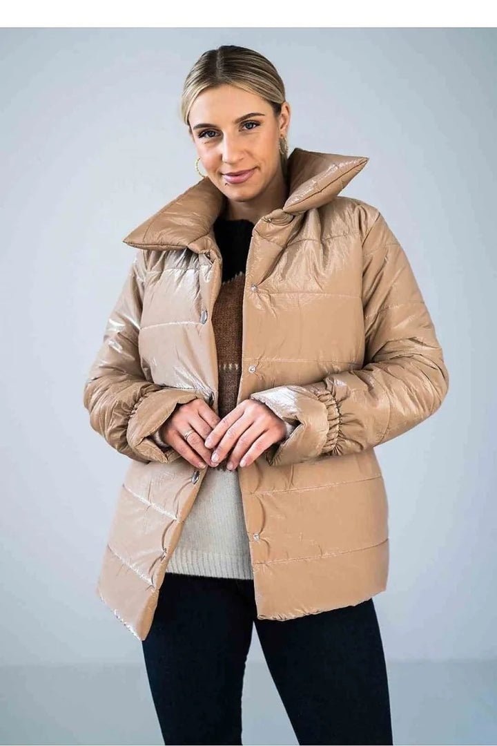 Woman wearing a shiny tan puffer jacket with a collared neckline and button closure, over a patterned sweater.