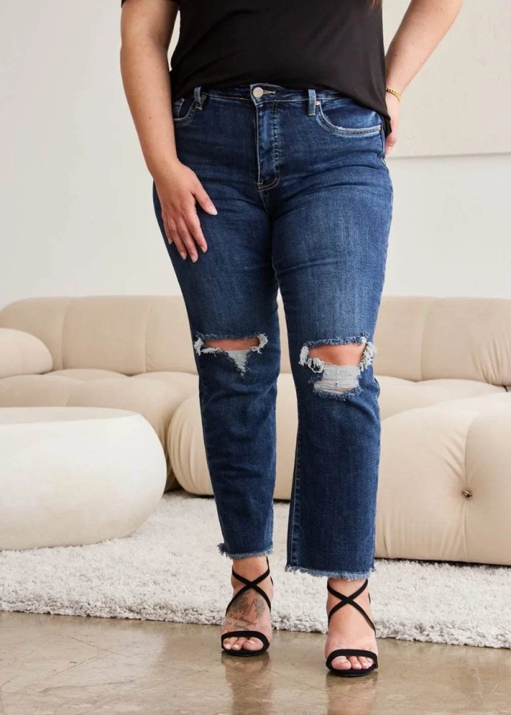 Dark wash distressed denim jeans with frayed hem and black strappy heels on model.