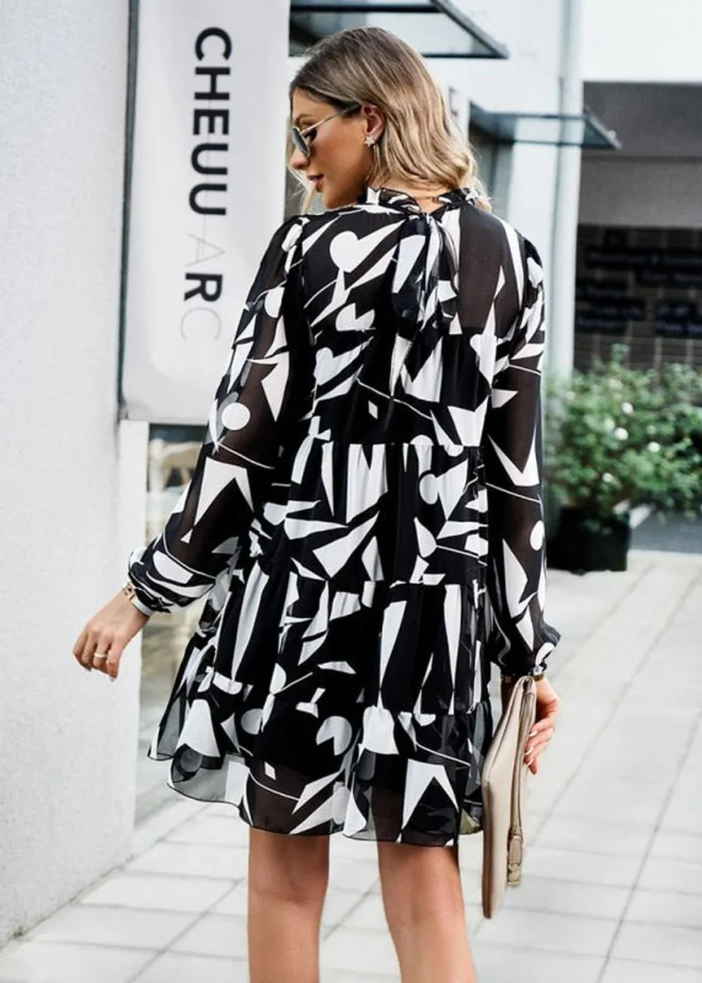 Black and white abstract print chiffon dress with tiered skirt and long sleeves, worn by a model.