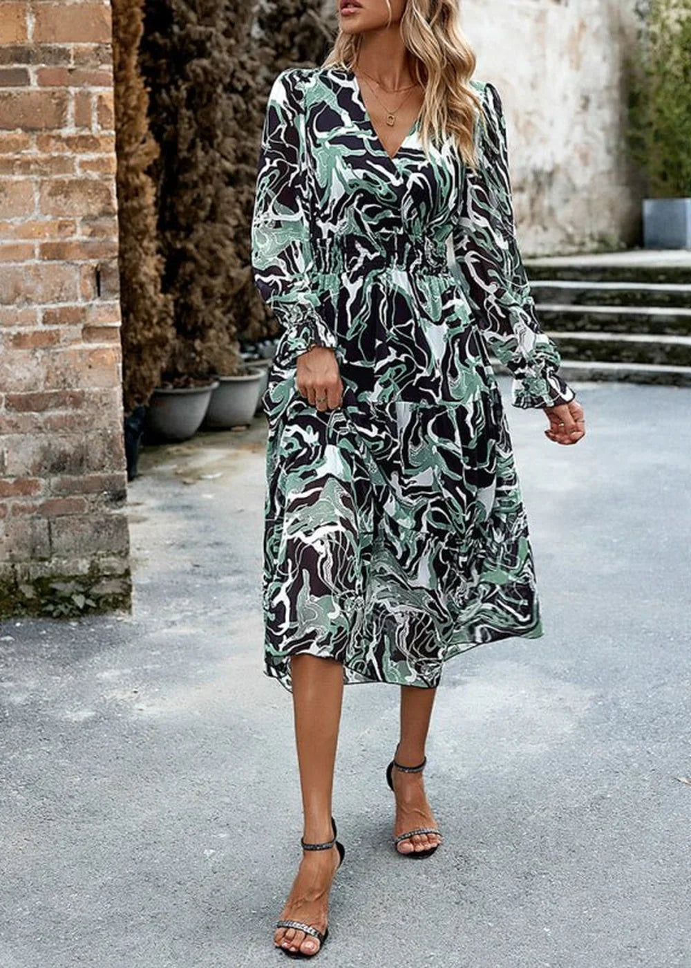 Woman in a green, black, and white abstract print midi dress with long sleeves and a tiered skirt.