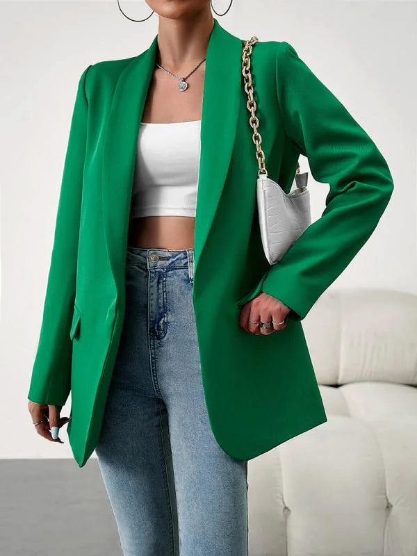 Emerald green blazer with gold chain detail and white textured bag on model.