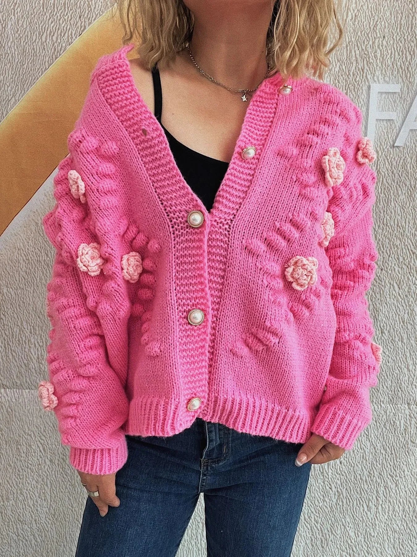 Pink knit cardigan with floral appliques and pearl buttons on a model.