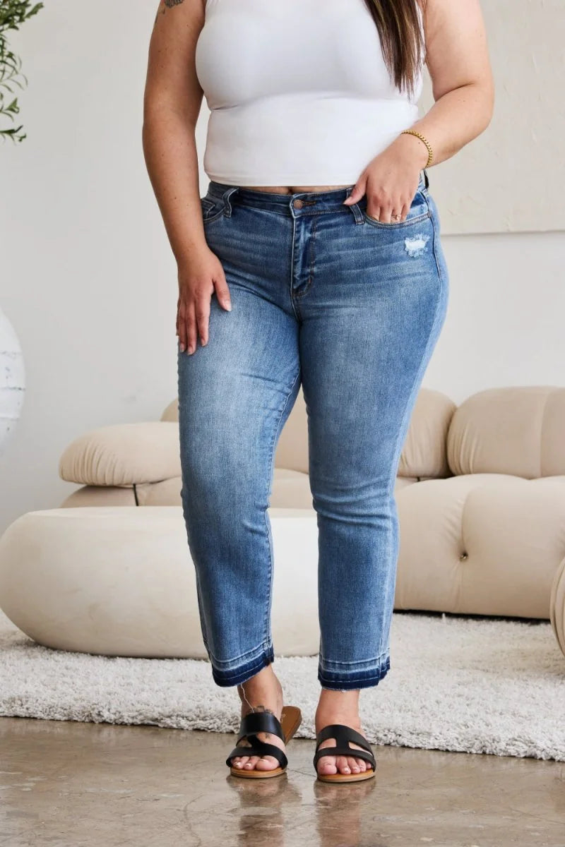 Medium wash denim jeans with distressed detail and frayed hem, worn by a model.