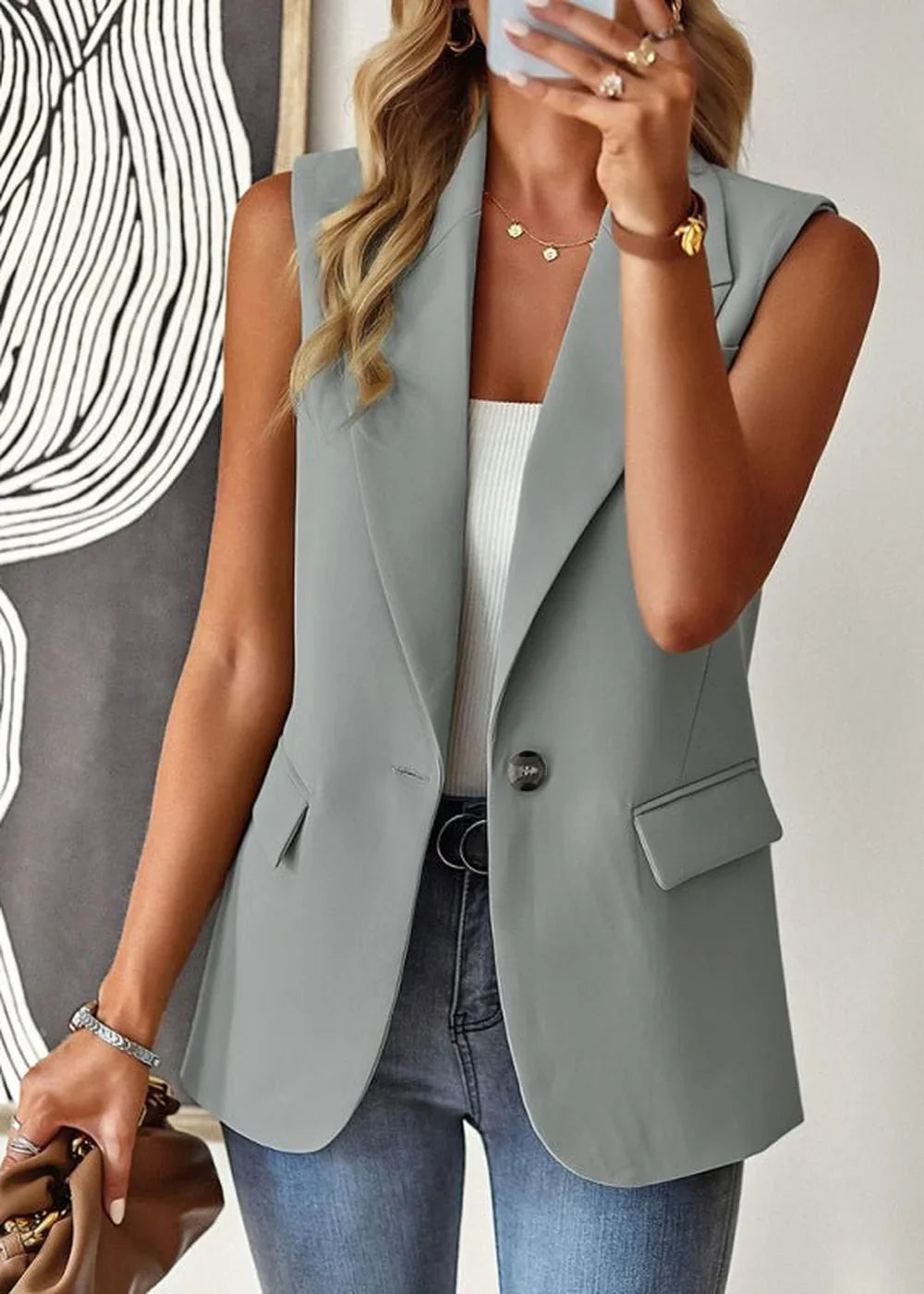 Grey sleeveless blazer with a single button closure and notched lapels, worn by a model over a white top.