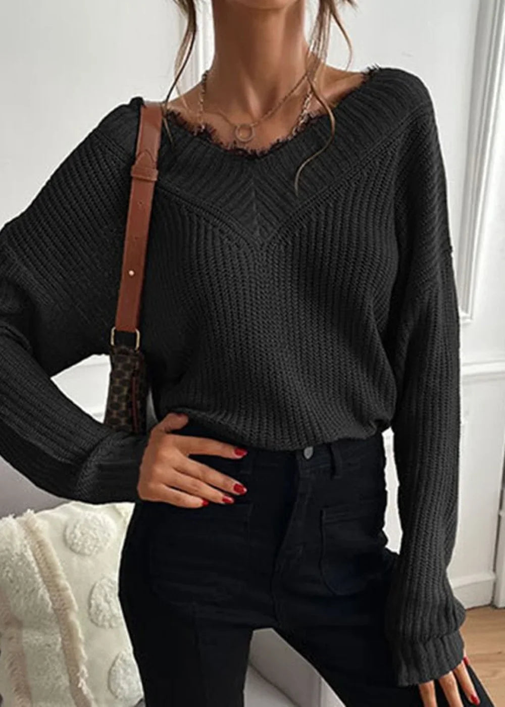 Black V-neck sweater with frayed neckline and ribbed texture, worn by a model with a brown crossbody bag.