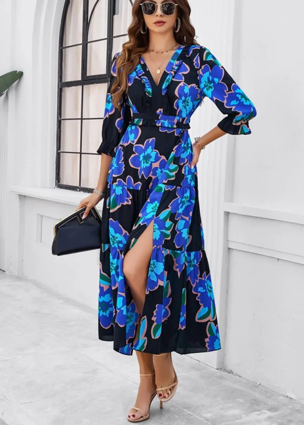 Woman in a navy blue floral print dress with a ruffled V-neck and high slit, holding a black clutch.