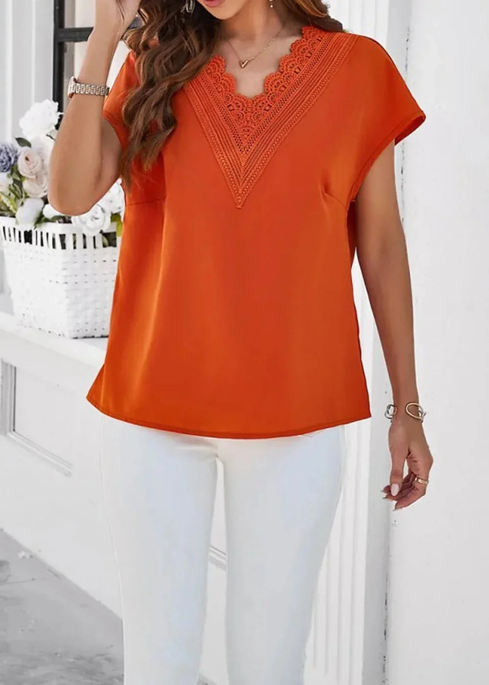 Orange v-neck top with lace trim and short sleeves, paired with white pants.