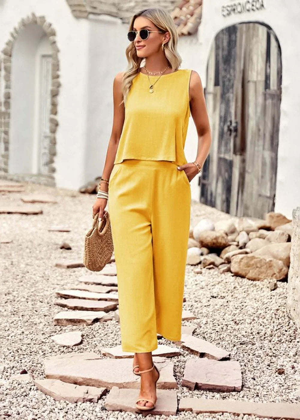 Woman in a bright yellow sleeveless crop top and wide-leg pants, holding a straw purse.