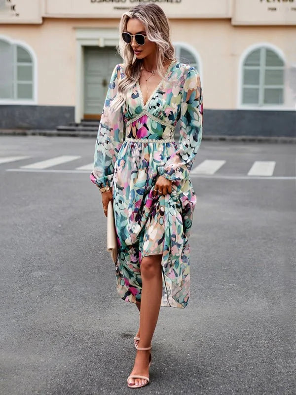 Flowy midi dress with abstract floral print in green, pink, and blue, featuring a V-neck and long sleeves.
