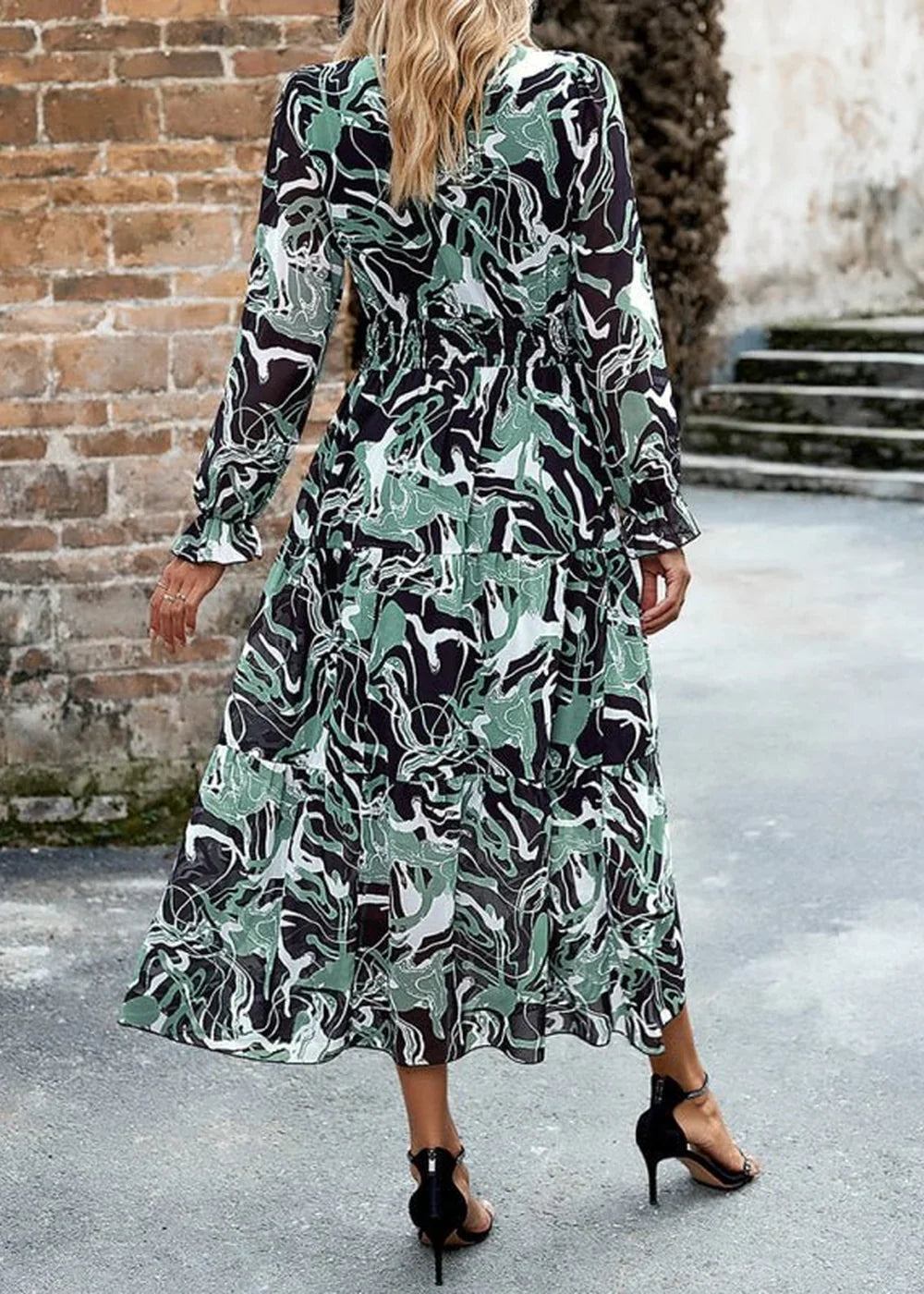 Flowy midi dress with abstract green, black, and white print, long sleeves, and tiered skirt.