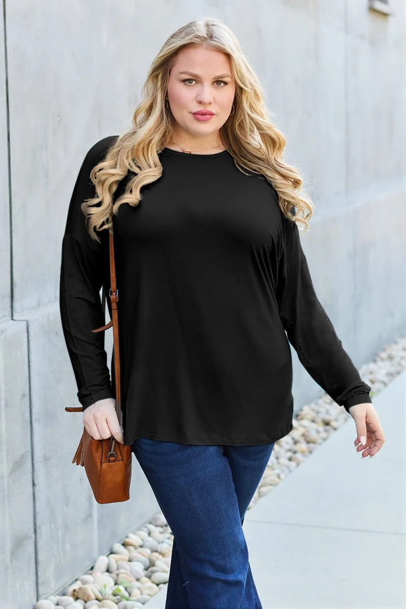 Woman in a black long-sleeve top and dark wash jeans, carrying a brown crossbody bag.