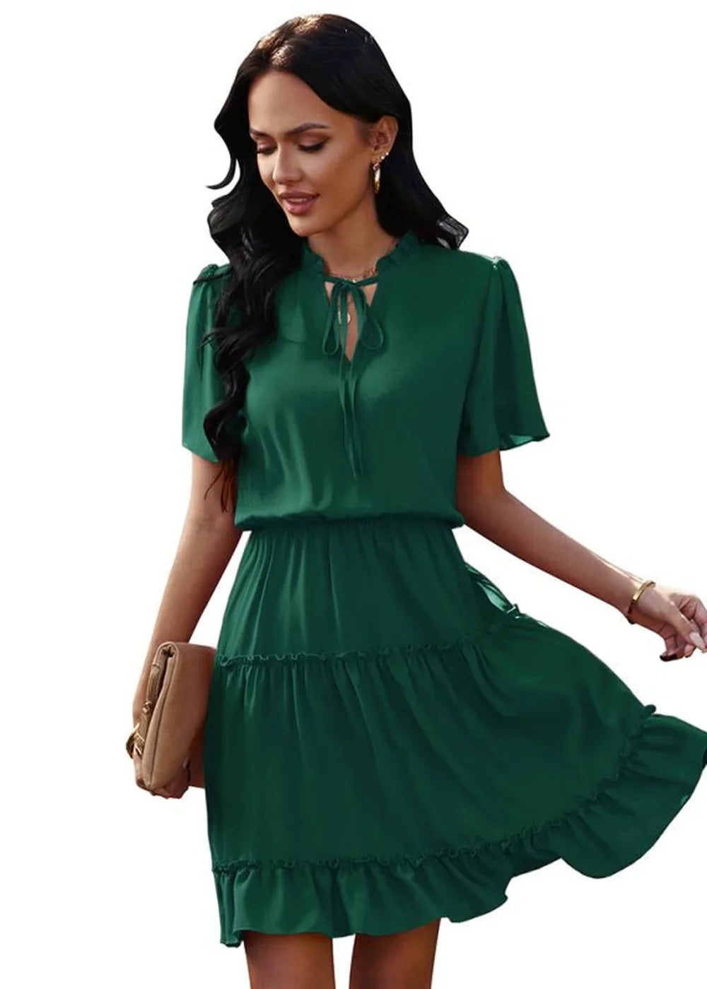Emerald green tiered ruffle dress with tie-neck detail and flutter sleeves, held by a model with a clutch.
