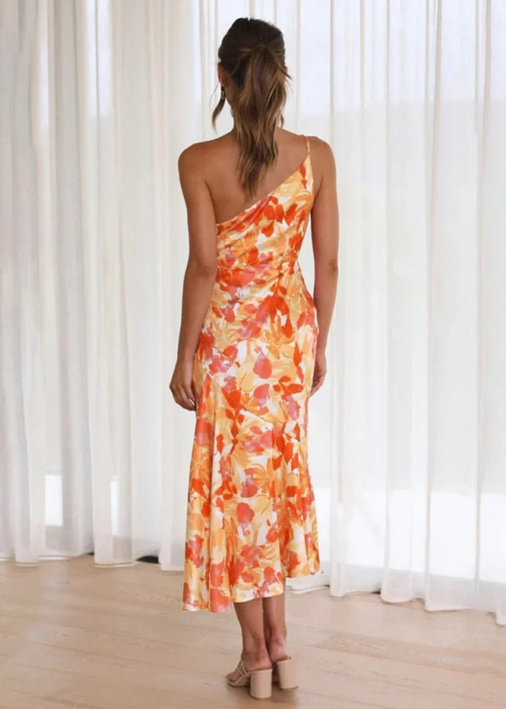 Orange and yellow floral print one-shoulder midi dress with ruched bodice and flowing skirt.