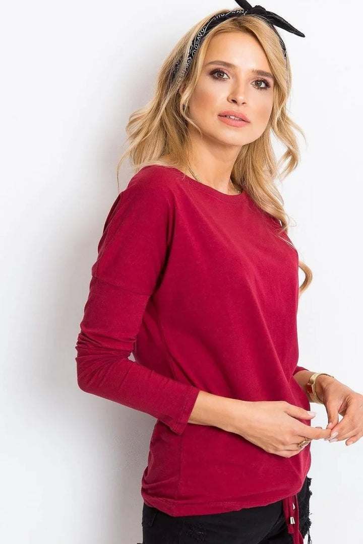 A woman's torso wearing a maroon long-sleeved top with a gold bracelet on her right wrist.