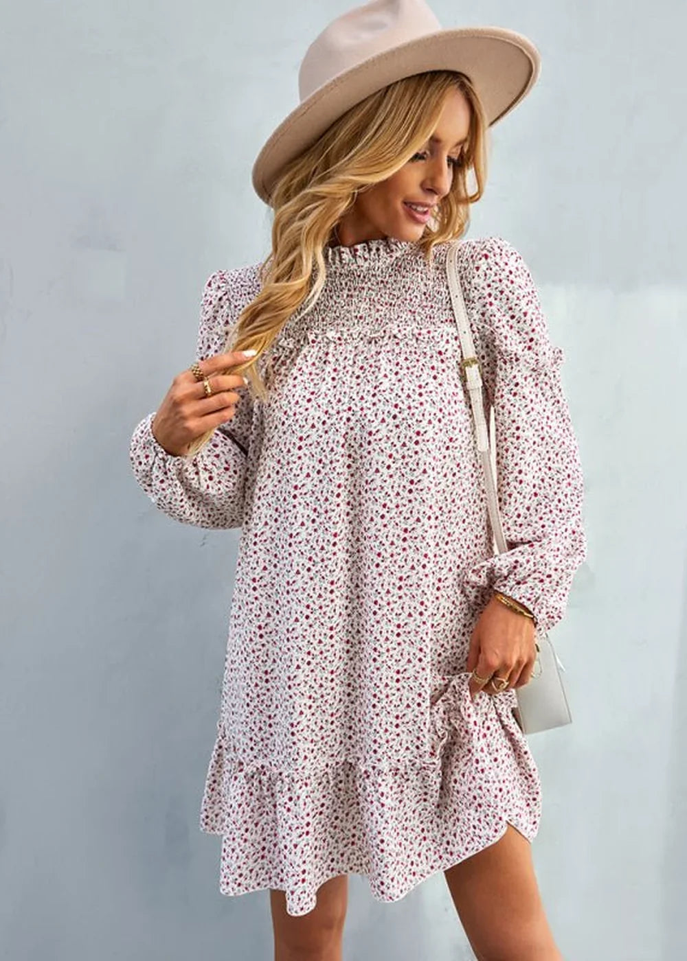 Woman in a white floral print dress with smocked neckline and ruffled hem, wearing a beige hat and crossbody bag.