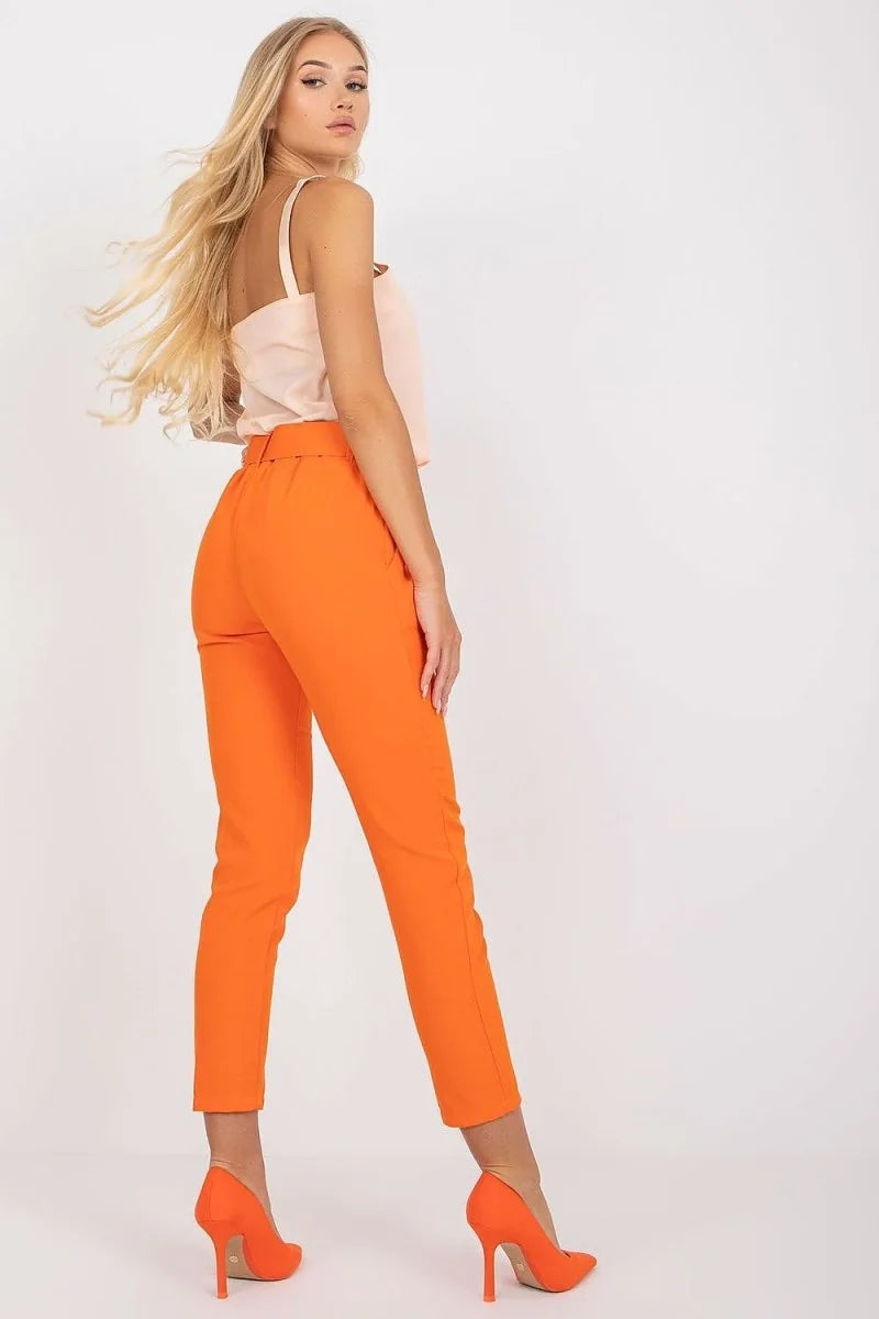 Orange high-waisted pants with a belt, worn by a model with a light pink top and orange heels.