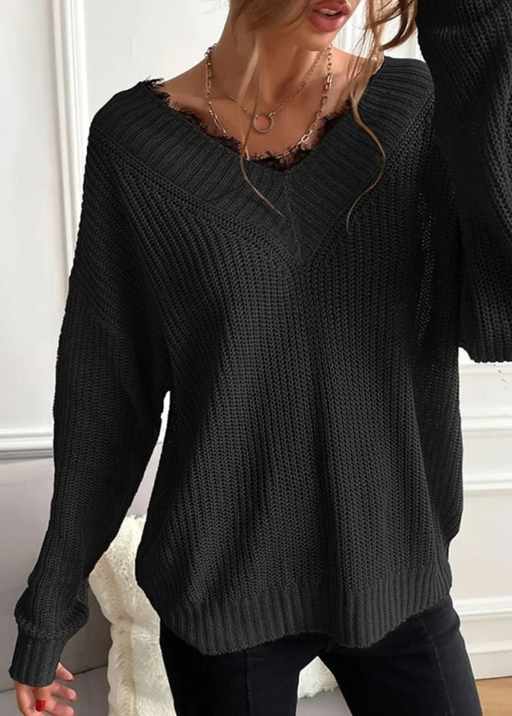 Black knit sweater with frayed V-neck and long sleeves on model.