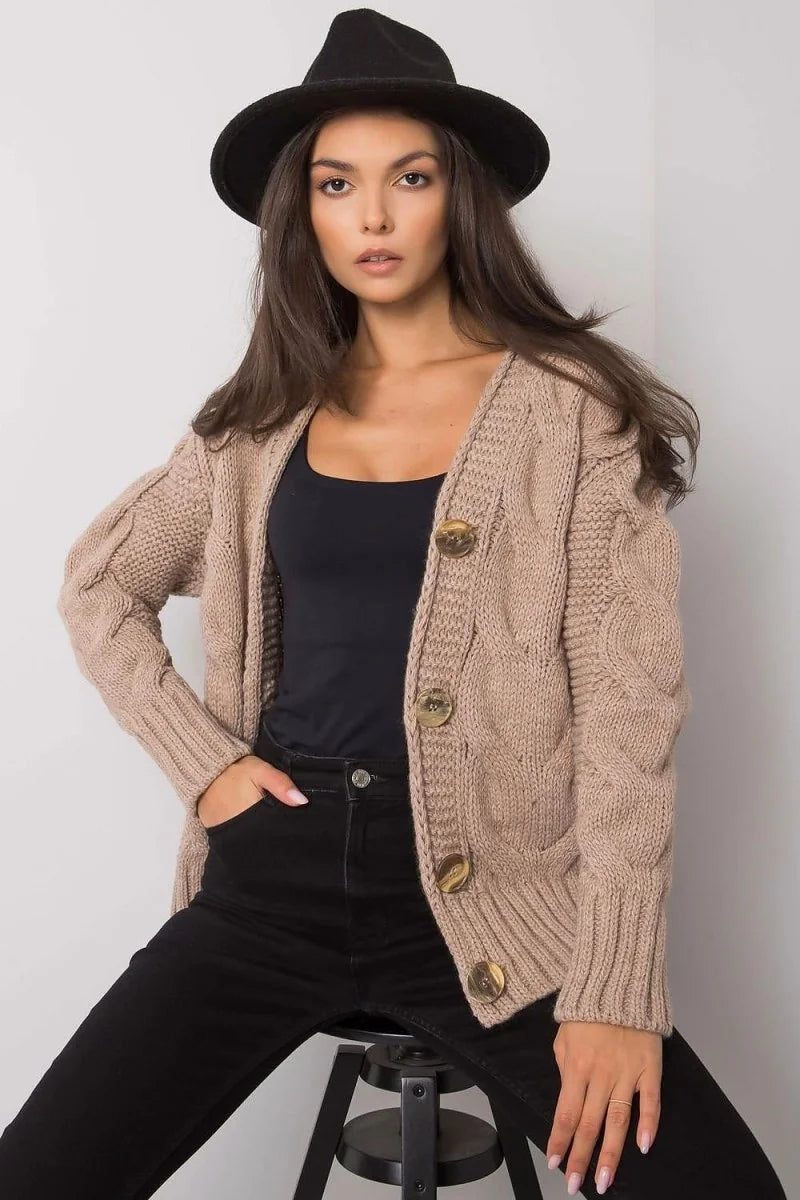 Beige cable knit cardigan with wooden buttons on a woman wearing a black hat and black jeans.