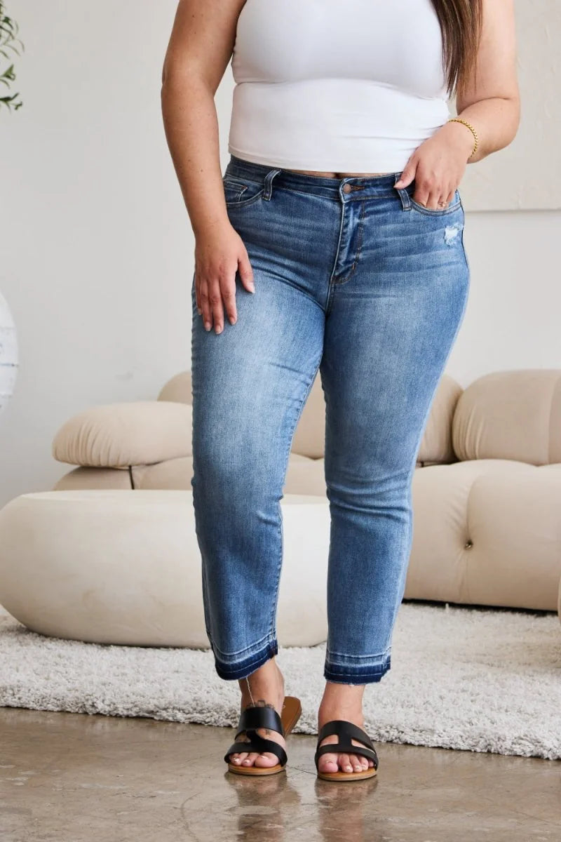 Medium wash distressed denim jeans with a frayed hem, on a model.