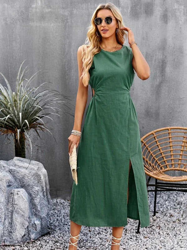 Woman in a green sleeveless midi dress with a high slit, holding a straw clutch.