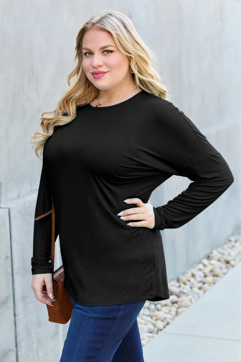 Woman wearing a black long-sleeved top with a round neck and blue jeans, holding a brown purse.