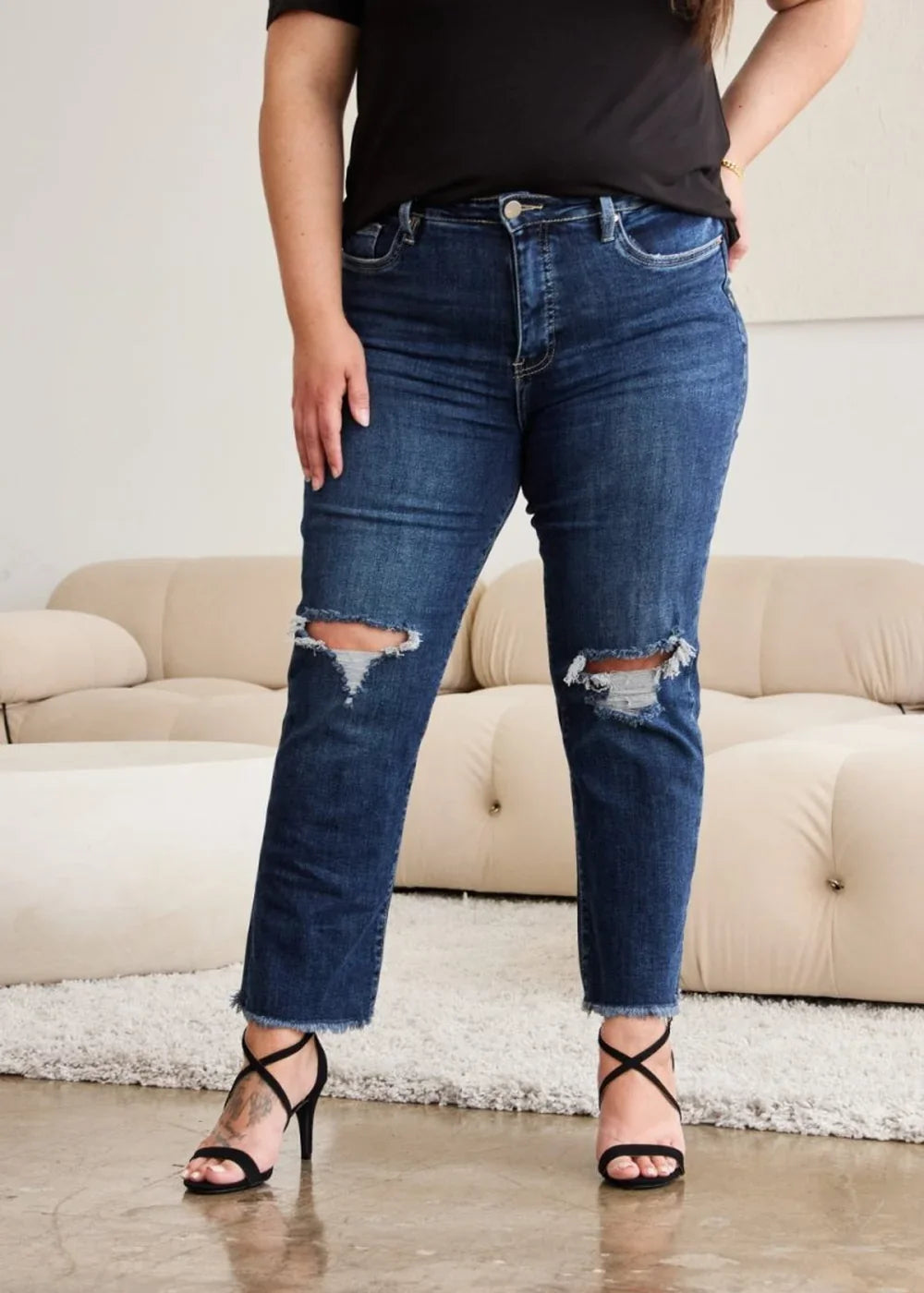 Dark wash, distressed denim jeans with a frayed hem and high waist, worn by a model with black strappy heels.