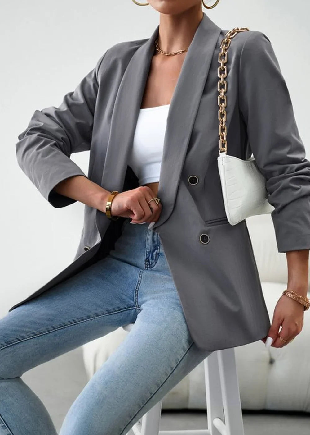 Gray double-breasted blazer with gold chain detail on white handbag, worn by a model.