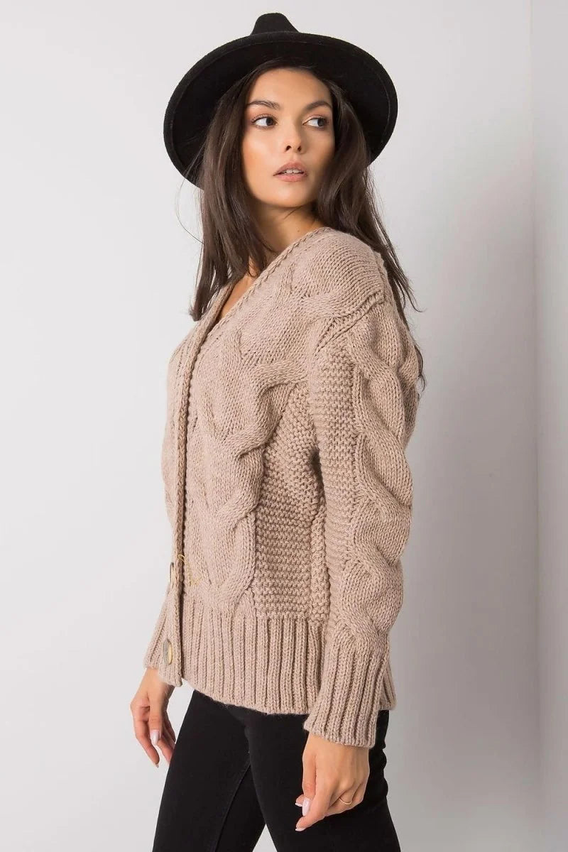 Beige cable-knit cardigan with gold buttons, worn by a model with a black hat.