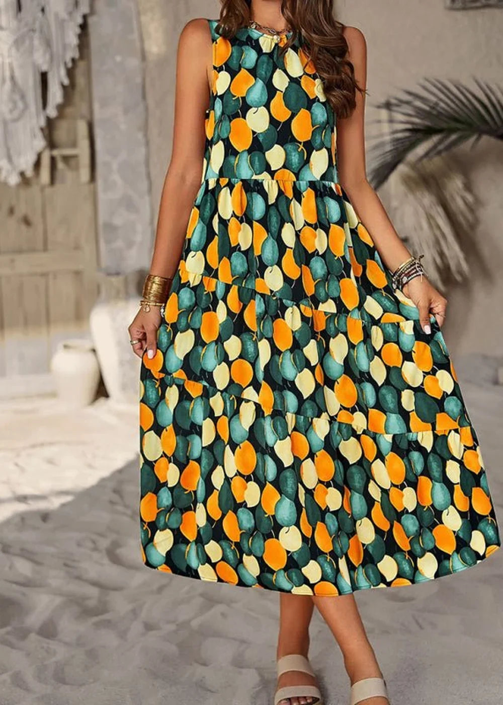 Sleeveless tiered midi dress with a dark green background and a scattered orange, teal, and cream leaf print.