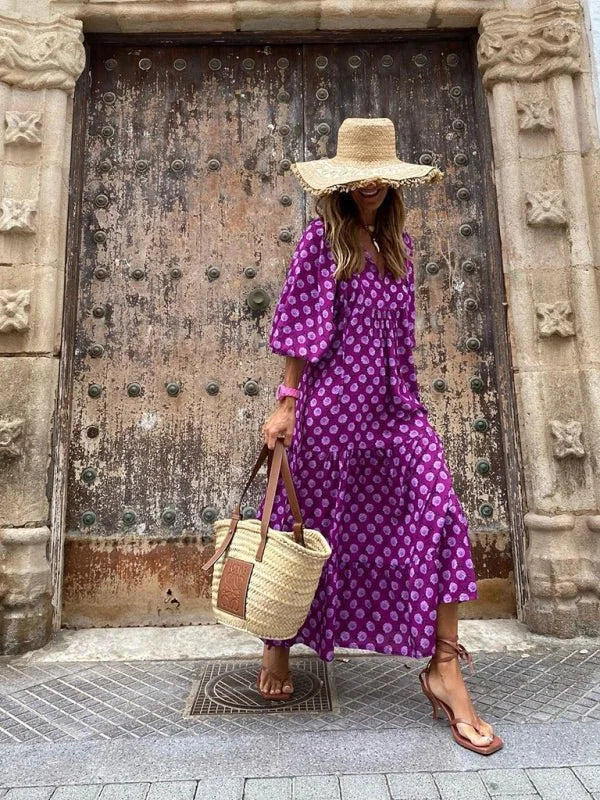 Purple polka dot maxi dress with straw hat and woven tote bag on model.
