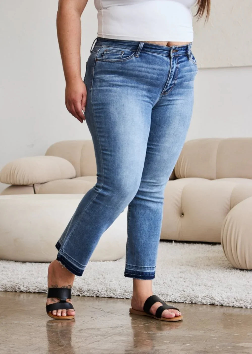 Light wash denim jeans with frayed hems, worn by a model with black sandals.