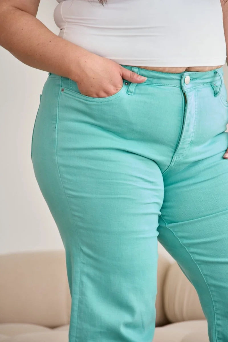 Close-up of light teal jeans with moderate stretch, showing a hand in the pocket and button closure.