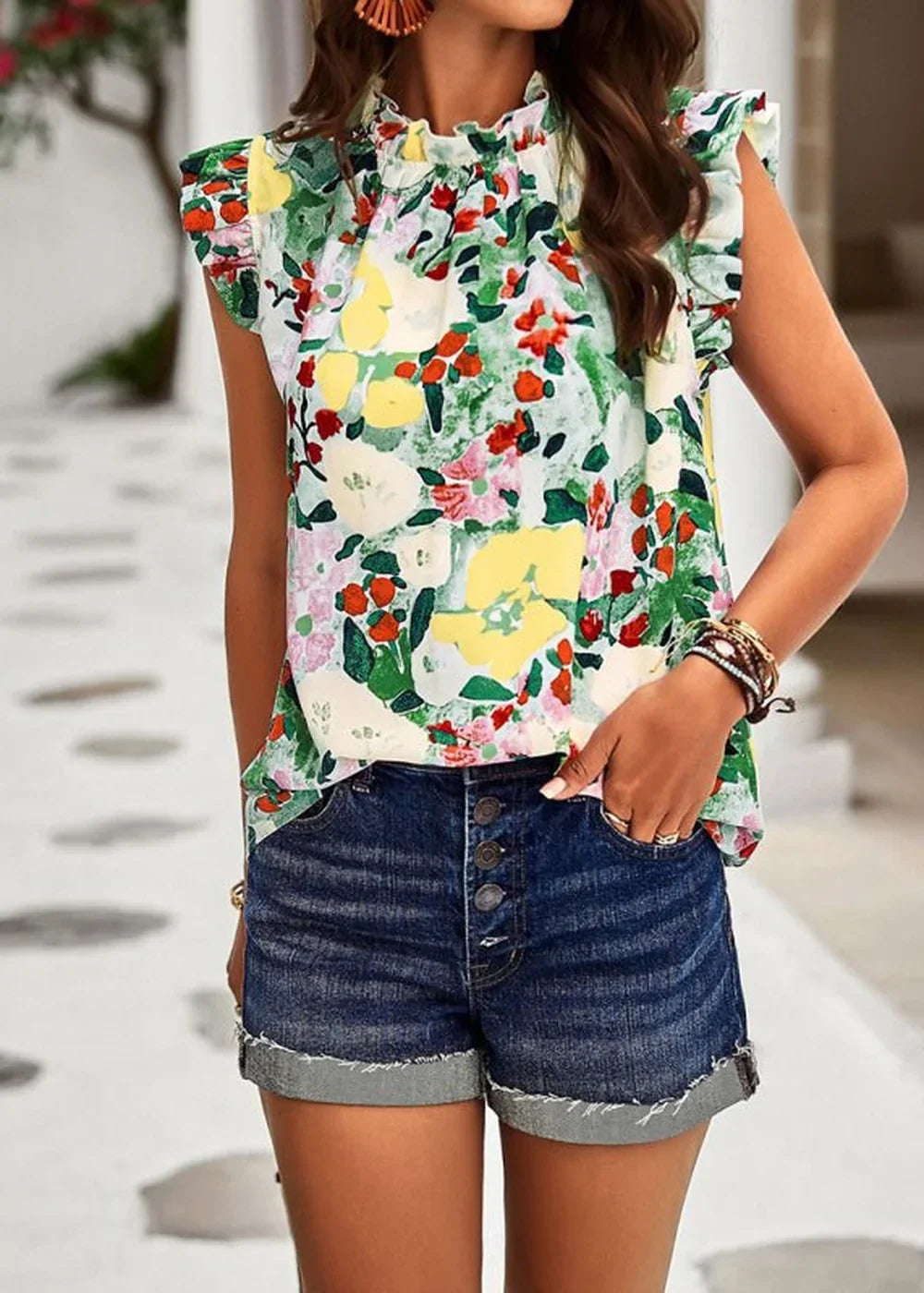 Woman in a floral print ruffled mock neck top and distressed denim shorts with a button fly.